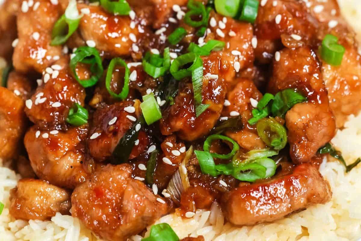 A close-up of a dish with glazed pork pieces on a bed of rice, topped with green onions and sesame seeds, reminiscent of inspired recipes you'd savor in your favorite restaurant.