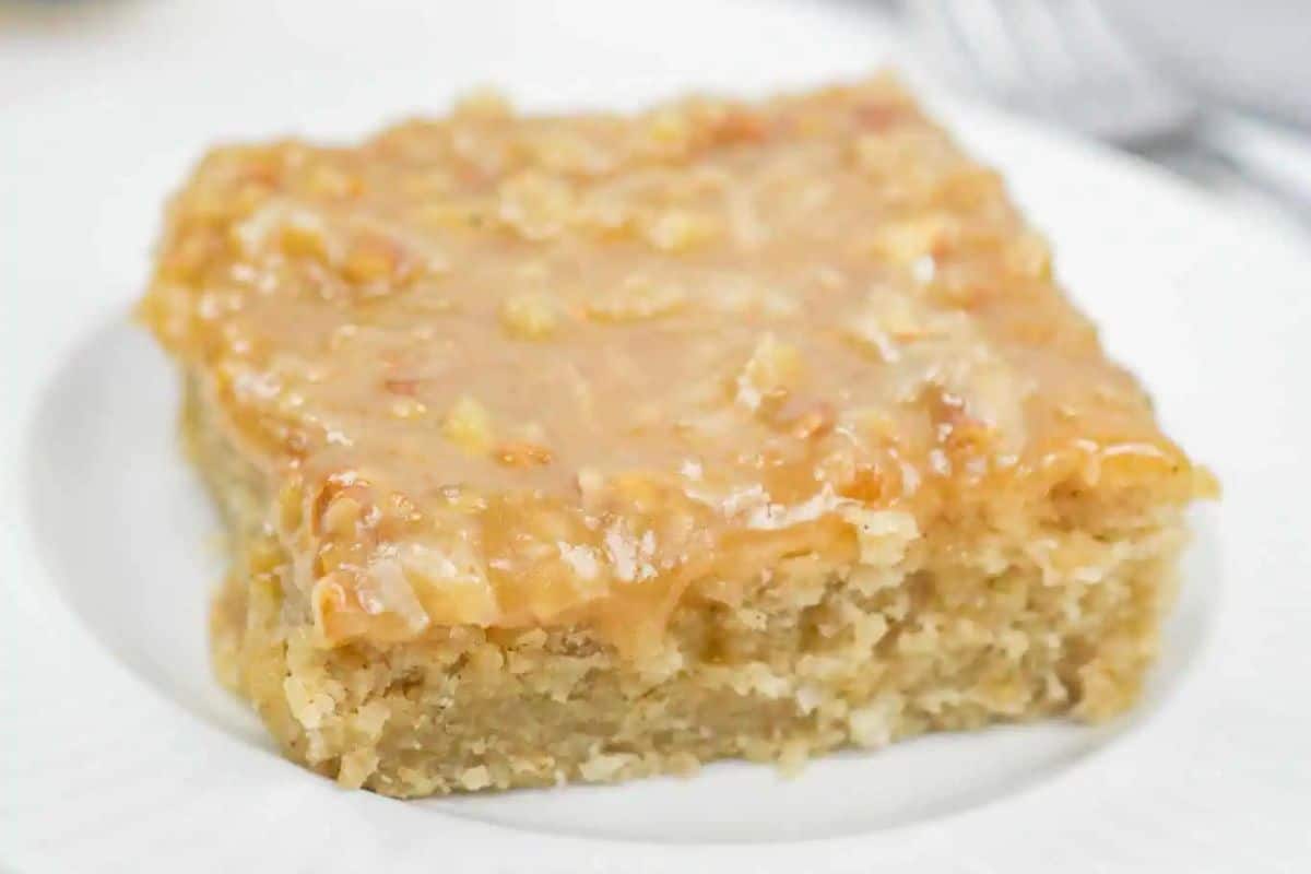 A square piece of oatmeal cake with a coconut glaze sits on a white plate, capturing the essence of vintage dishes and classic recipes.
