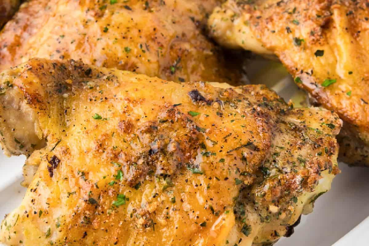 Close-up of juicy chicken thighs with golden, crispy skin and visible herbs on a white plate—perfect inspiration for delicious chicken thigh recipes.