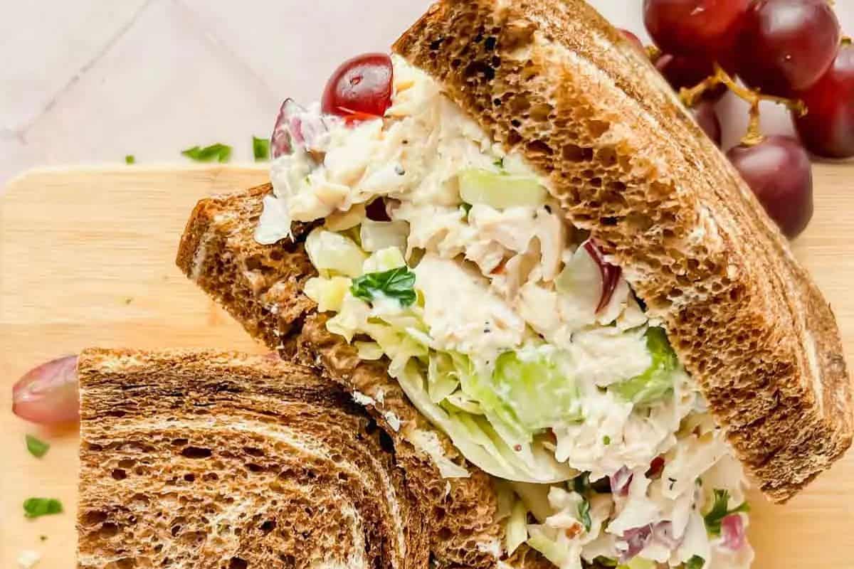 Chicken salad sandwich with lettuce and grape pieces on marbled rye bread, placed on a wooden board with red grapes in the background—a delicious twist on restaurant inspired recipes you can make at home.