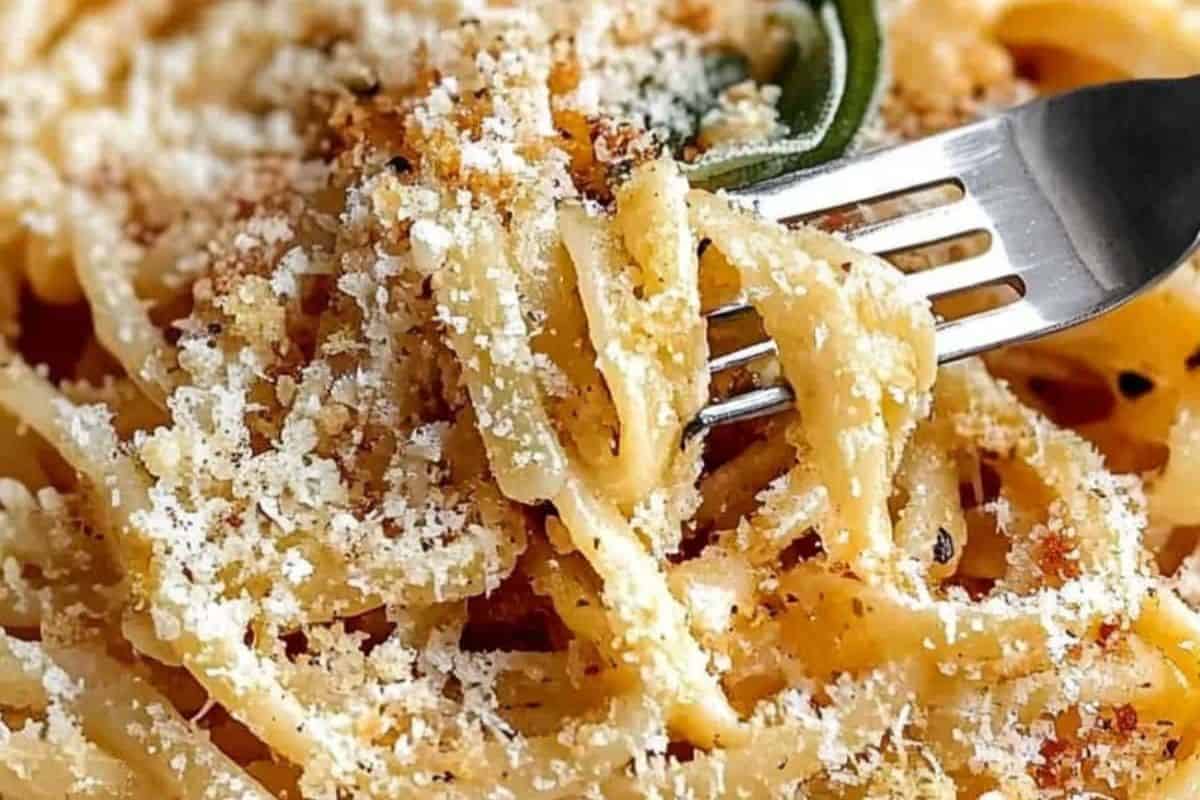 A close-up of Spaghetti with Cacio e Pepe being twirled on a fork. The pasta is coated in a creamy, light-colored sauce with visible grated cheese and black pepper.