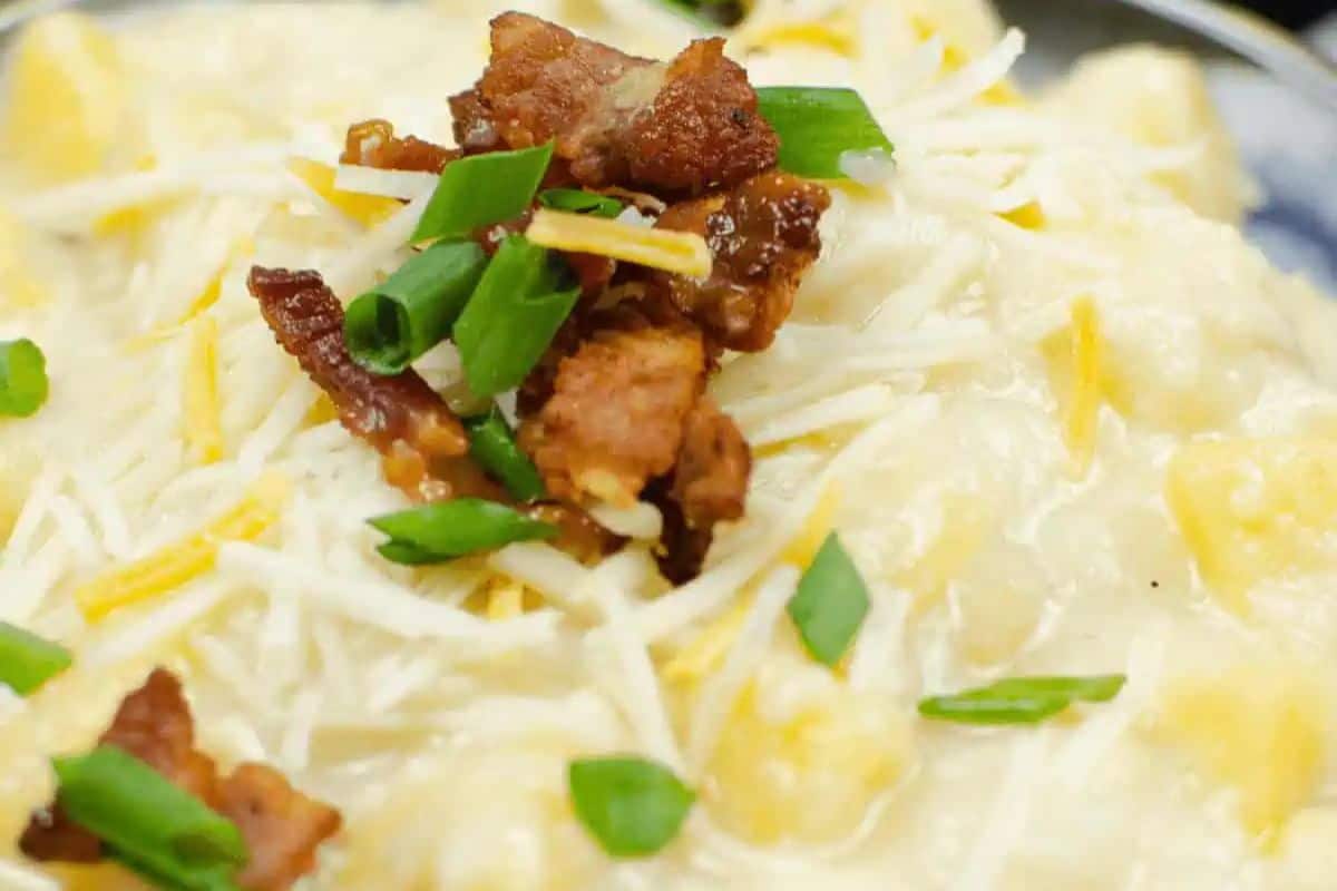 A close-up of creamy cheesy potato soup, topped with shredded cheese, bacon pieces, and chopped green onions—a game changing dish you'll want to repeat in your Instant Pot recipes.