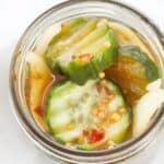 A jar of Refrigerator Bread and Butter Pickles in brine, featuring sliced pickles with visible mustard seeds, spices, and onion slices.