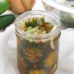 A glass jar with fresh cucumber and an onion in the background.