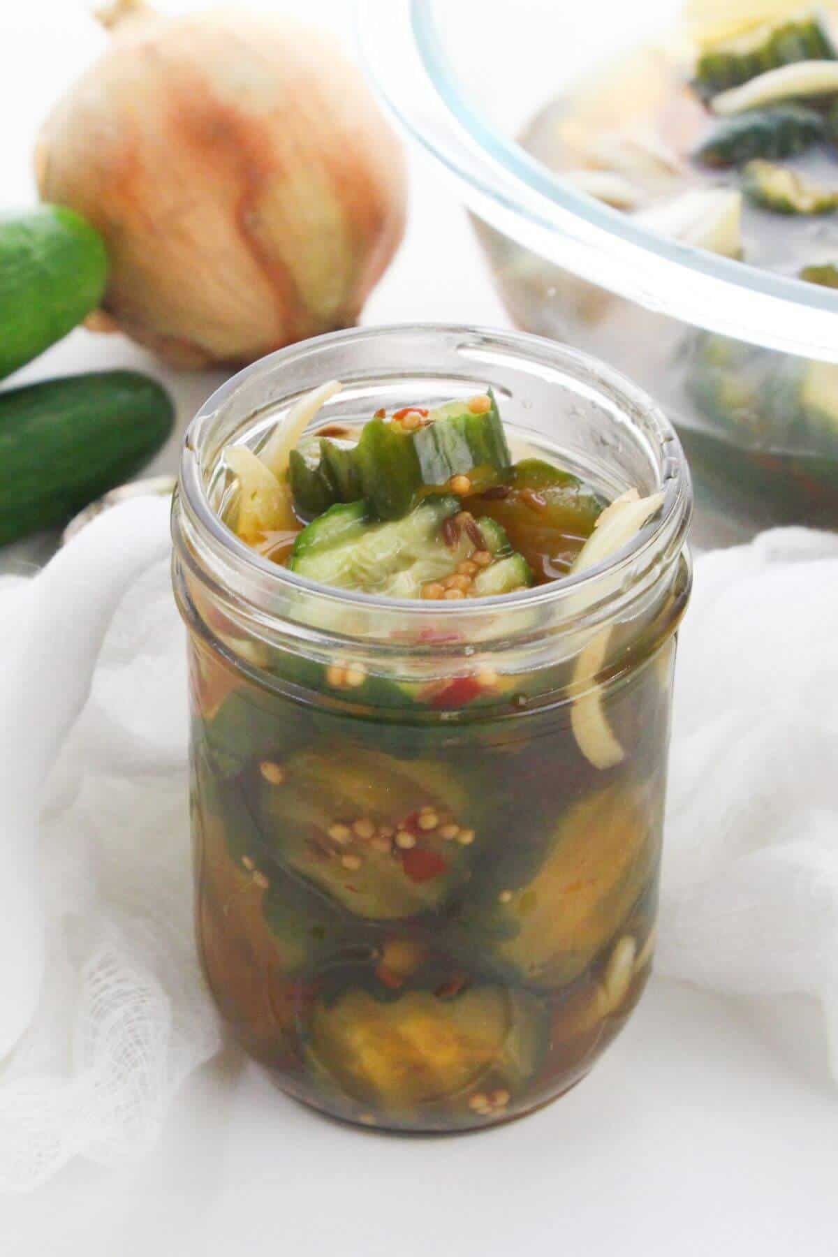 A glass jar with fresh cucumber and an onion in the background.
