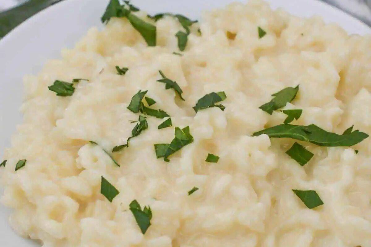 A close-up overhead shot of a white plate filled with creamy, pale-colored risotto, garnished with fresh green parsley leaves.