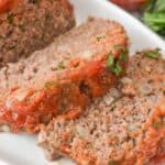 The meat on a white plate, garnished with chopped herbs and served with a side of sauce.