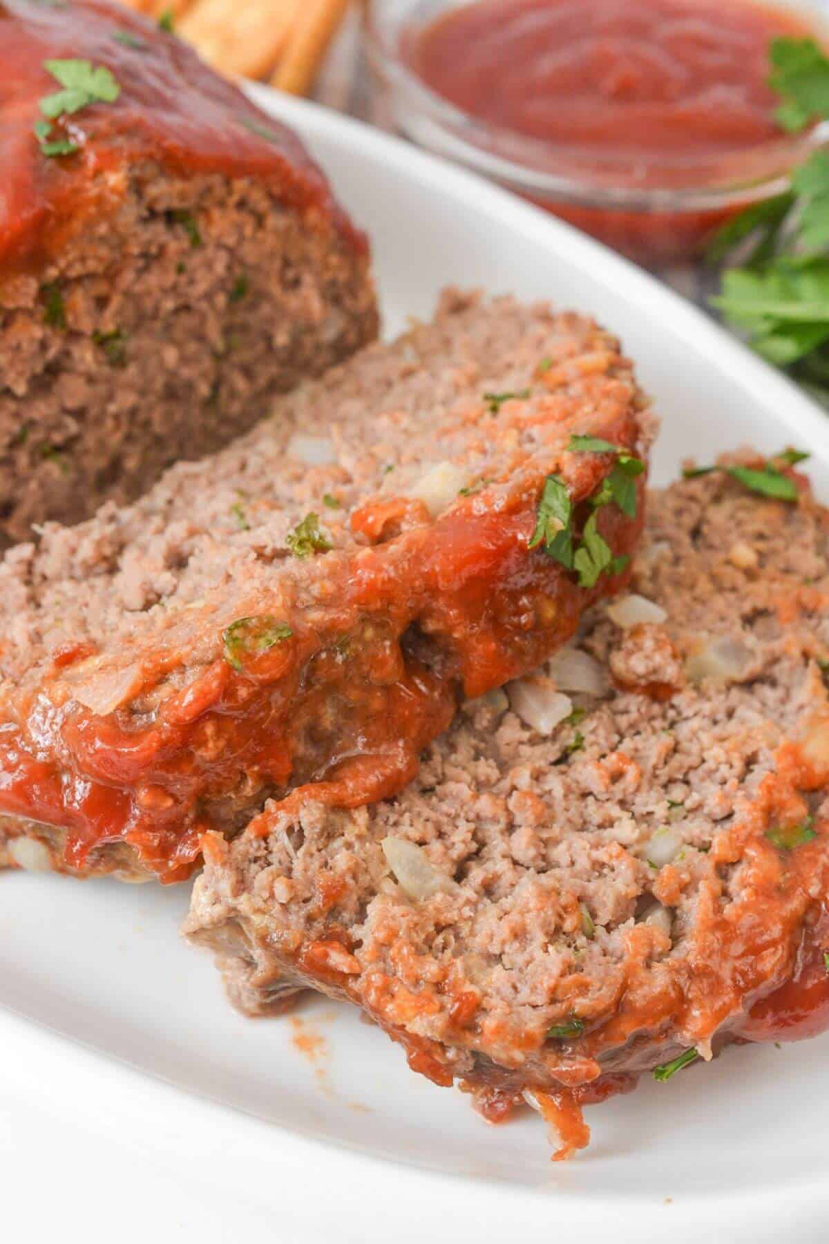 The meat on a white plate, garnished with chopped herbs and served with a side of sauce.