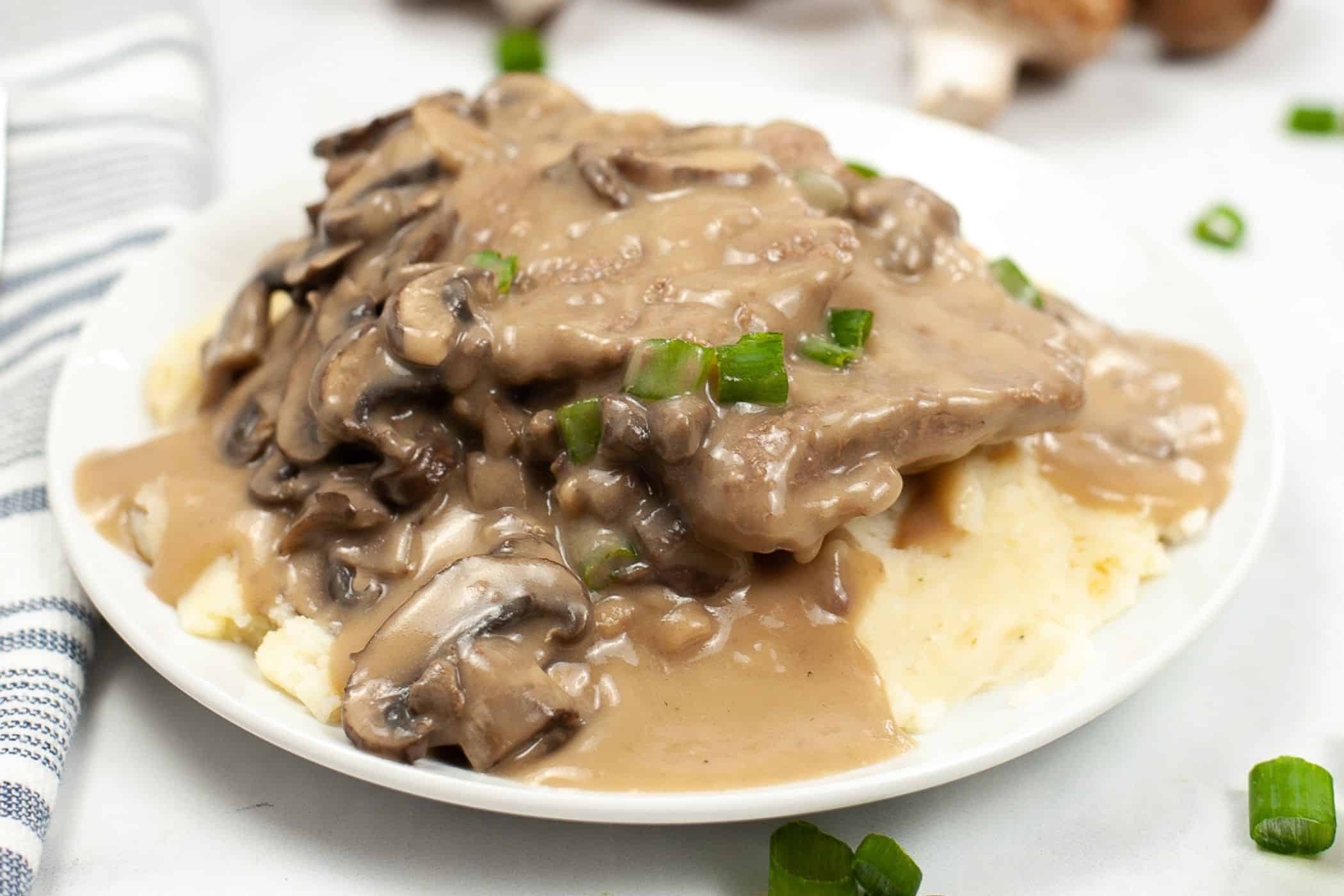 A plate of mashed potatoes topped with salisbury steak, sautéed mushrooms, creamy brown gravy, and chopped green onions—perfect for busy weeknights or when you’re searching for comforting cube steak recipes.