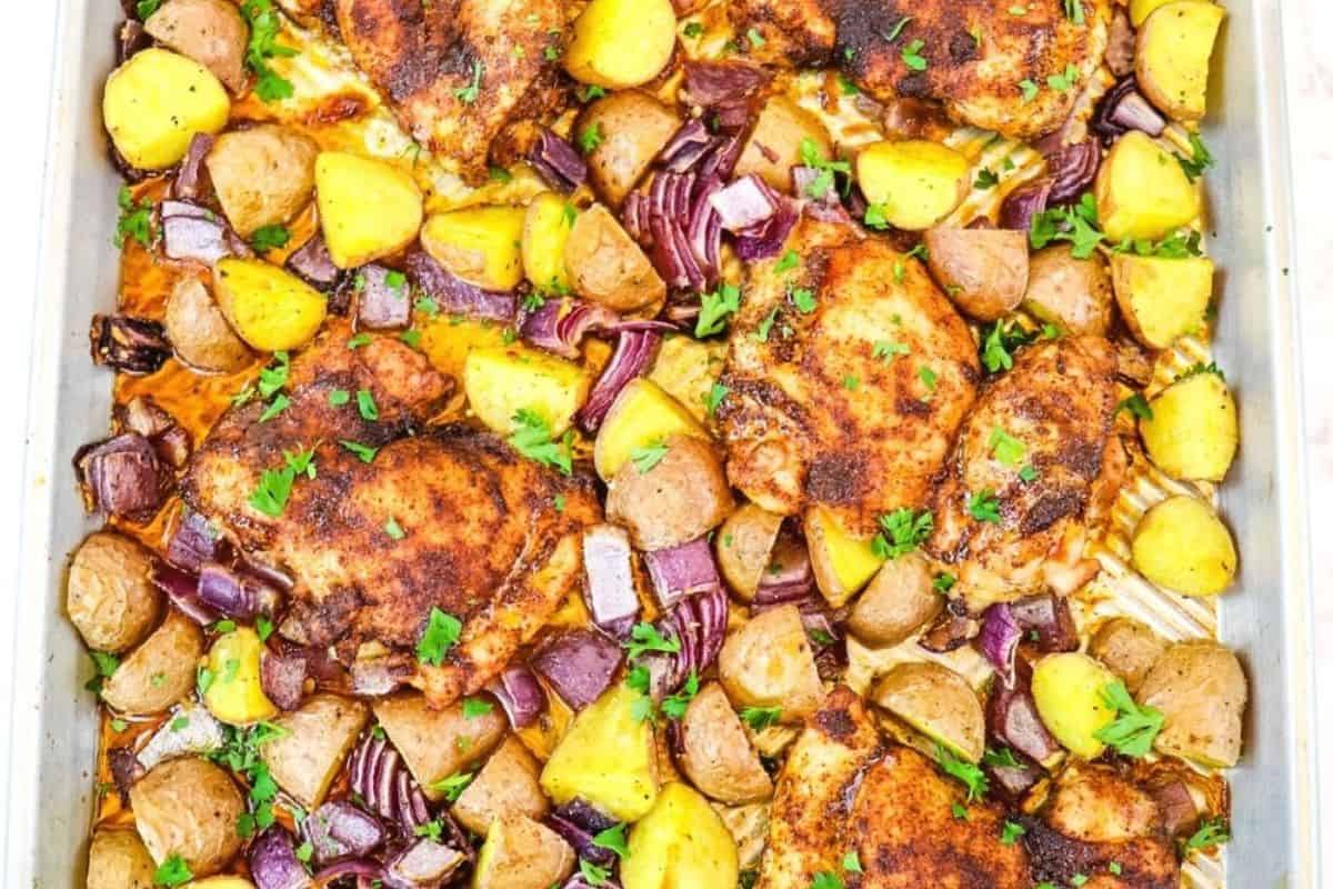 Sheet pan with juicy chicken thighs, chopped yellow and red potatoes, and red onions, garnished with fresh parsley—a flavorful addition to your favorite chicken thigh recipes.