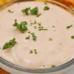 A small glass bowl of creamy Sheetz Boom Boom Sauce, garnished with chopped parsley, surrounded by crinkle-cut fries on a white plate.