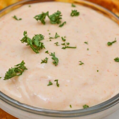 A small glass bowl of creamy Sheetz Boom Boom Sauce, garnished with chopped parsley, surrounded by crinkle-cut fries on a white plate.