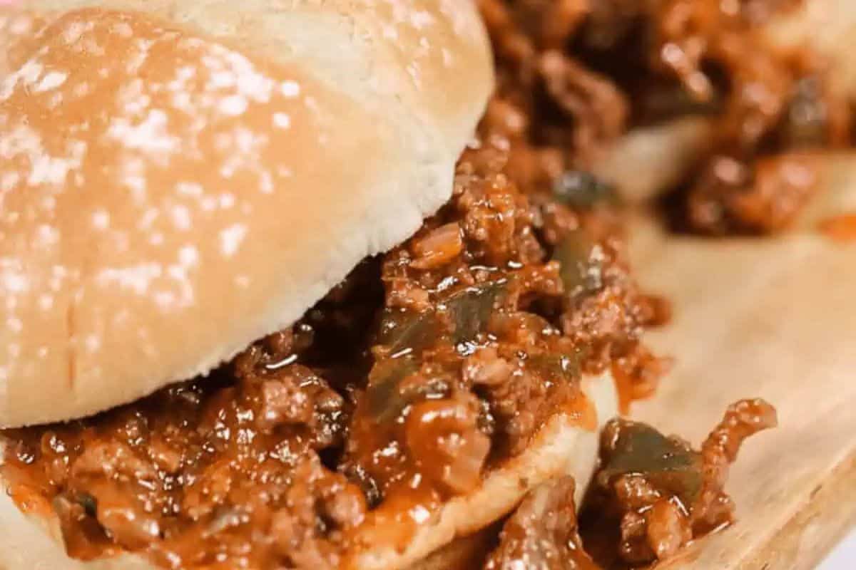  A soft hamburger bun is filled with a loose, saucy mixture of browned ground beef, diced onions in a reddish-brown tomato-based sauce.