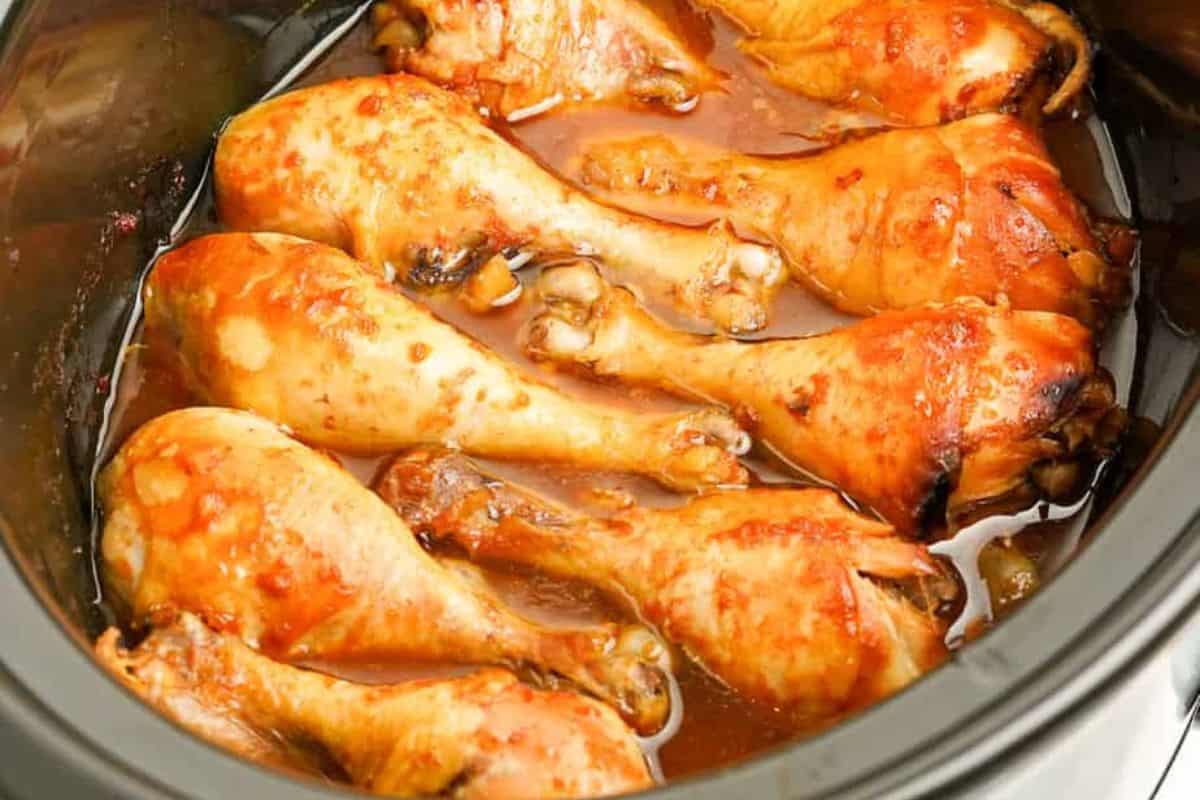 Chicken drumsticks cooked in a slow cooker with a reddish sauce, arranged closely together in the pot—one of those finger licking chicken recipes that's sure to please.