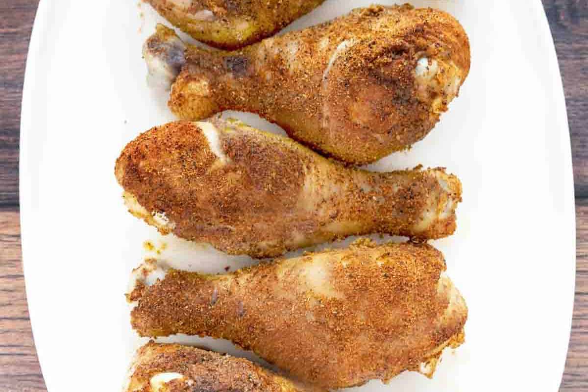 Five seasoned and cooked chicken drumsticks are arranged in a row on a white plate, viewed from above—a finger licking addition to your collection of easy chicken recipes.
