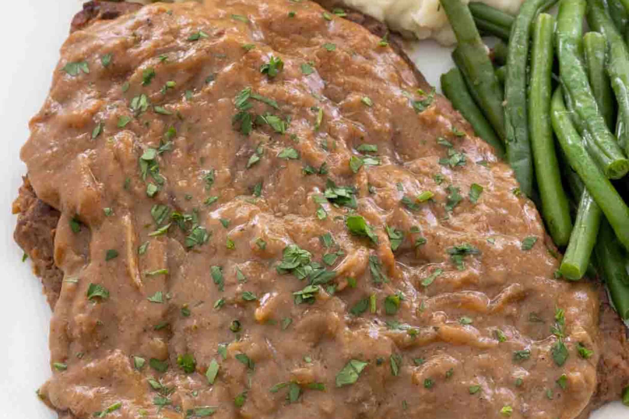 Perfect for busy weeknights, this breaded meat dish is a classic among cube steak recipes, topped with brown gravy and chopped herbs, and served alongside green beans and creamy mashed potatoes.