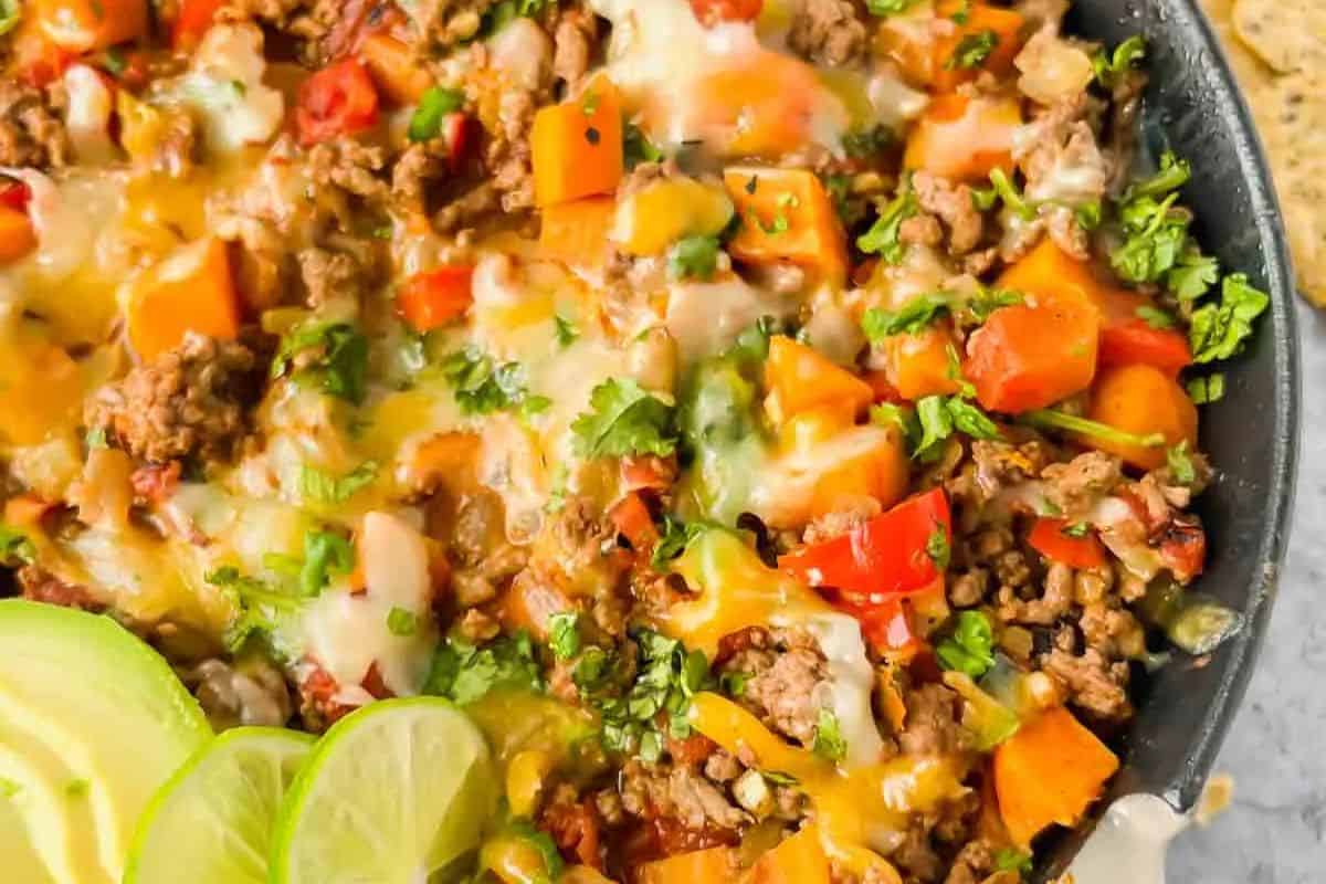 A delicious skillet dish of cheesy beef with diced vegetables, garnished with chopped herbs and lime slices—perfect for two.