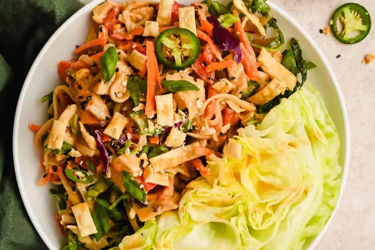 A colorful salad in a bowl features restaurant-style flair with lettuce, julienned carrots, strips of tofu, sliced jalapeños, and a creamy dressing.