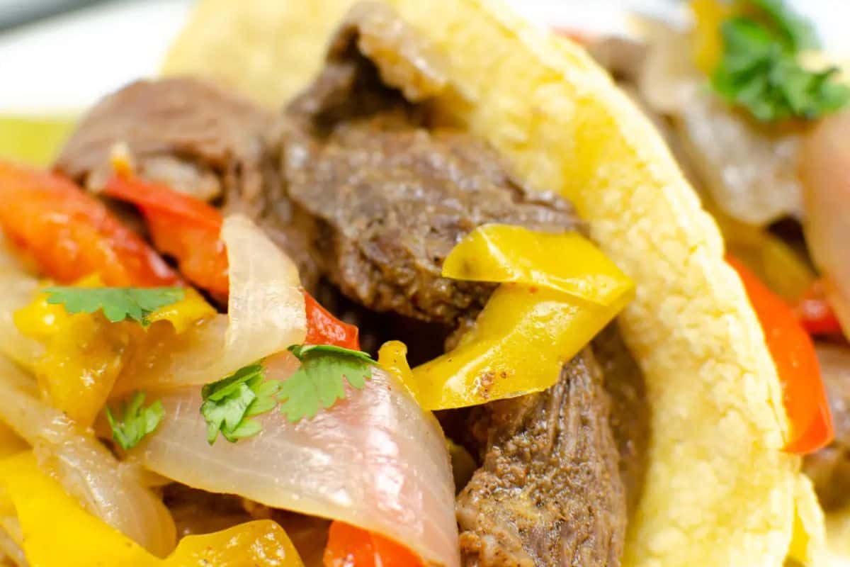 Close-up of a game changing taco filled with beef, sliced red and yellow bell peppers, onions, and topped with fresh cilantro.
