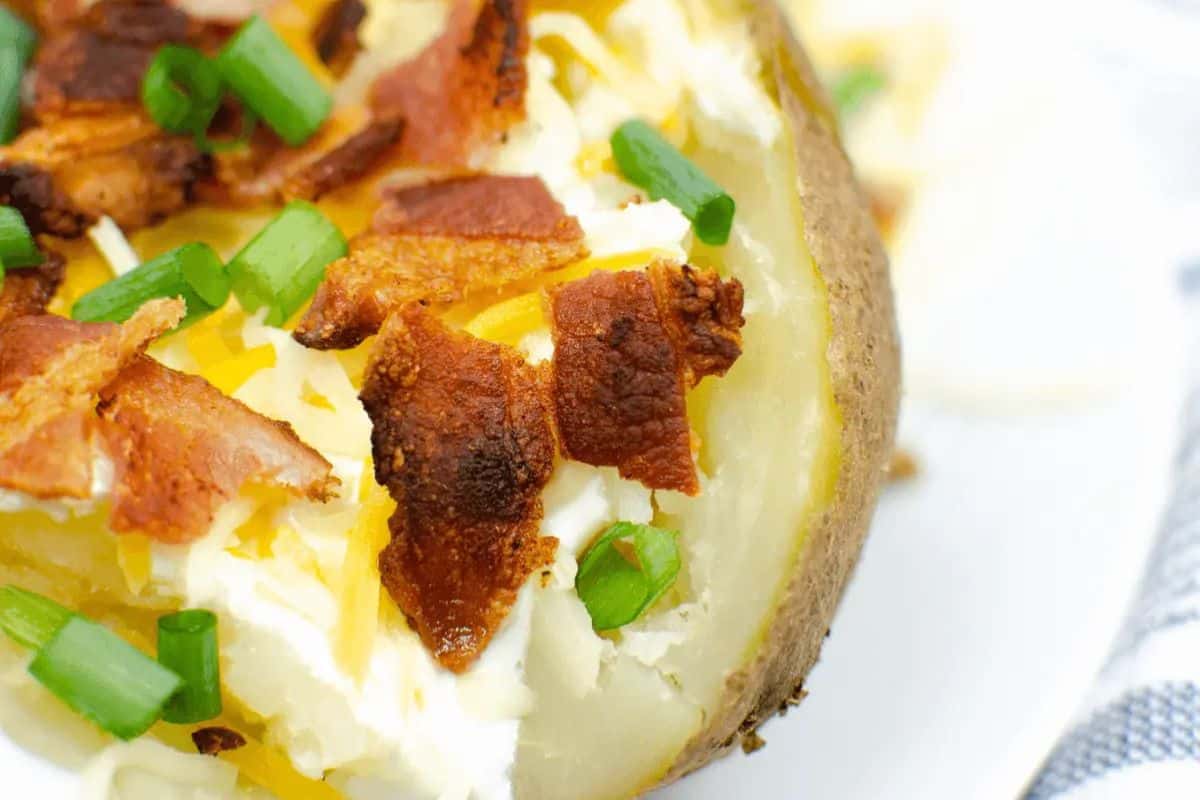 A game changing baked potato topped with sour cream, shredded cheese, bacon pieces, and chopped green onions—a dish you'll want to repeat.