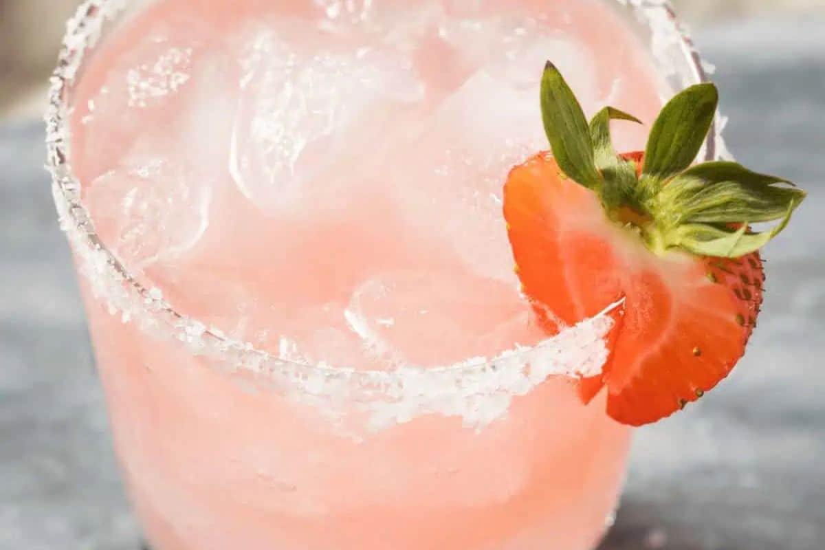 A glass of strawberry margarita over ice with a salted rim, garnished with a fresh strawberry slice—a modern take on timeless cocktails everyone should know.