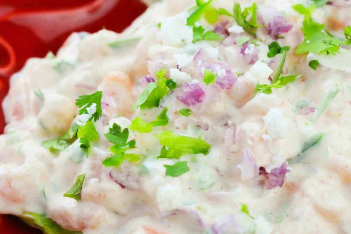  A close-up of Taco Shrimp Salad in a red bowl. The creamy salad features cooked shrimp, diced red onion, chopped cilantro, and a creamy white dressing.