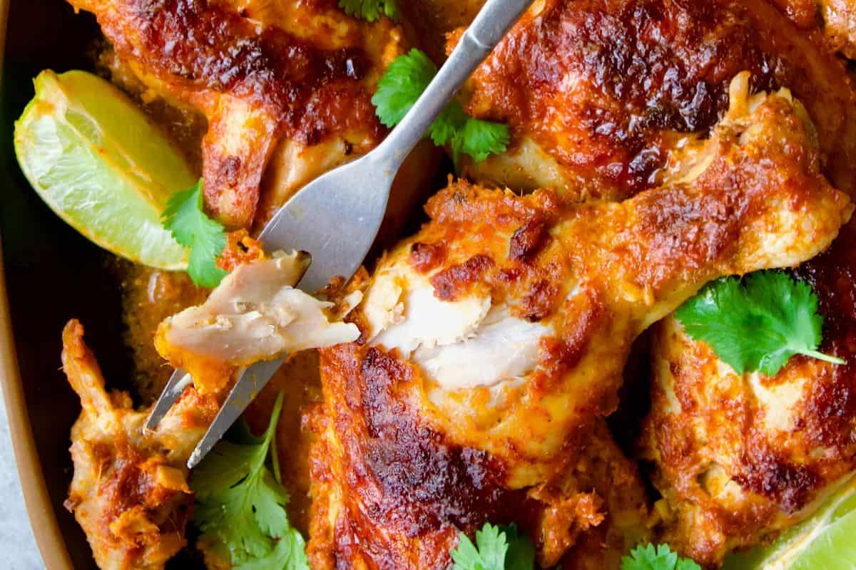 Close-up of finger licking chicken pieces garnished with cilantro, with a fork taking a bite and lime wedges on the side—a delicious highlight for your favorite chicken drumstick recipes.
