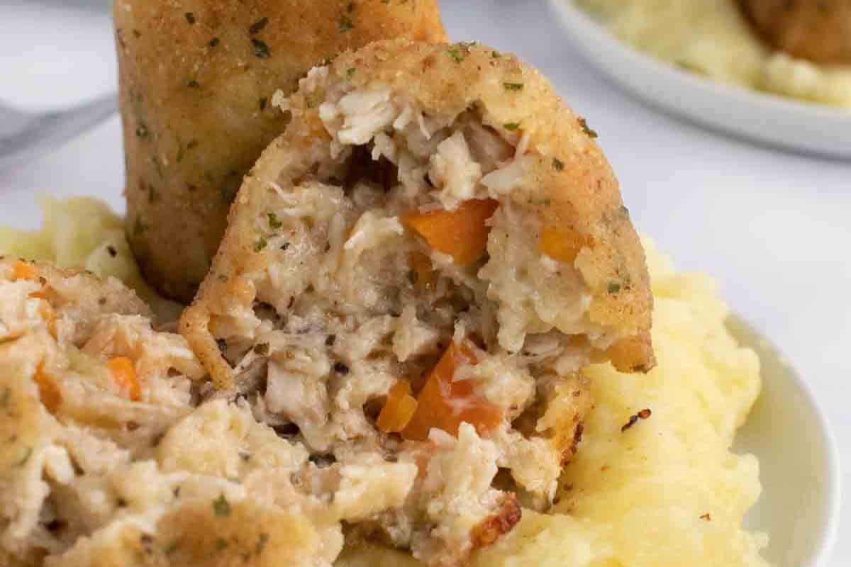 A breaded, stuffed croquette cut open to show a filling of shredded chicken and vegetables, served on a bed of mashed potatoes—bringing classic dishes to your table with comfort and flavor.