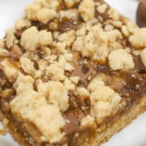 A close-up of a dessert bar with a crumbly oat topping and a visible caramel layer, resting on a light surface—perfect for fans of indulgent desserts and easy caramel recipes.