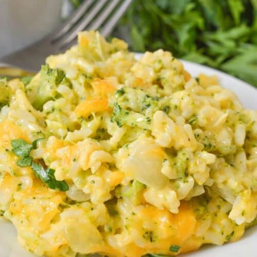 A plate of Velveeta broccoli rice casserole sits on a white surface, with visible pieces of broccoli, rice, creamy melted cheese, and a sprinkle of parsley.
