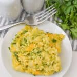 A plate of velveeta broccoli rice casserole sits next to a fork, salt and pepper shakers, and a bunch of fresh parsley on a striped cloth.