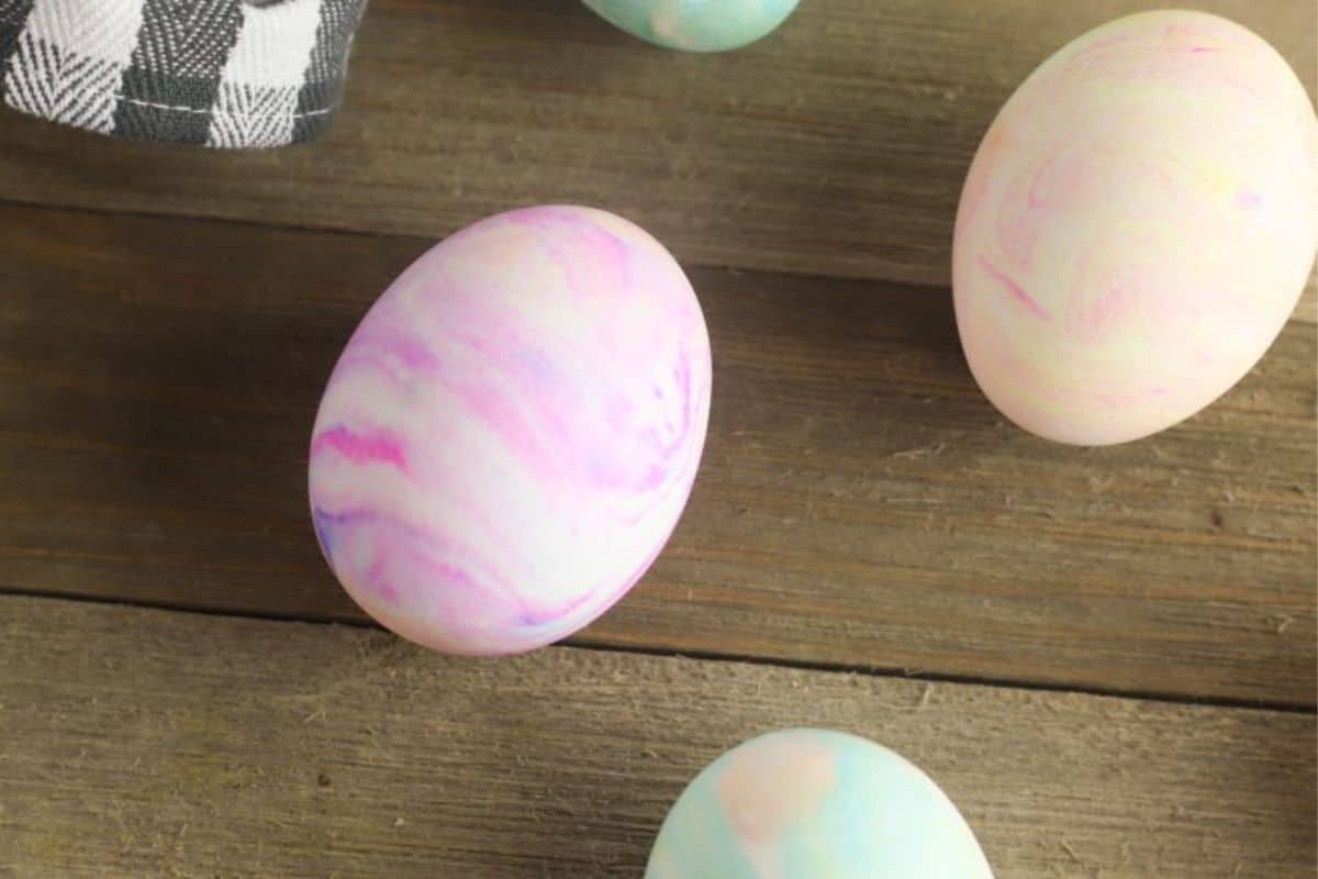 Four pastel marbled Easter eggs rest on a wooden surface next to a black and white checkered cloth, perfect for Easy Easter Ideas or inspiring your next round of Easter Egg Decorating.