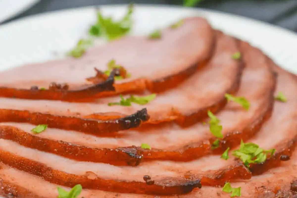 Thin, evenly sliced ham is beautifully caramelized on the edges, with a glossy glaze and a sprinkling of fresh herbs for a festive touch. This image showcases the crisp edges and juicy interior that make air fryer hams so appealing. It’s a perfect visual for a modern, no-fuss holiday ham.
