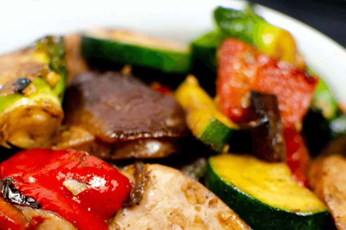 A colorful medley of roasted zucchini, bell peppers, mushrooms, and juicy chicken apple sausage slices fills the plate with vibrant, savory goodness. The vegetables are lightly charred for added flavor, making this a healthy and satisfying one-pan dish.