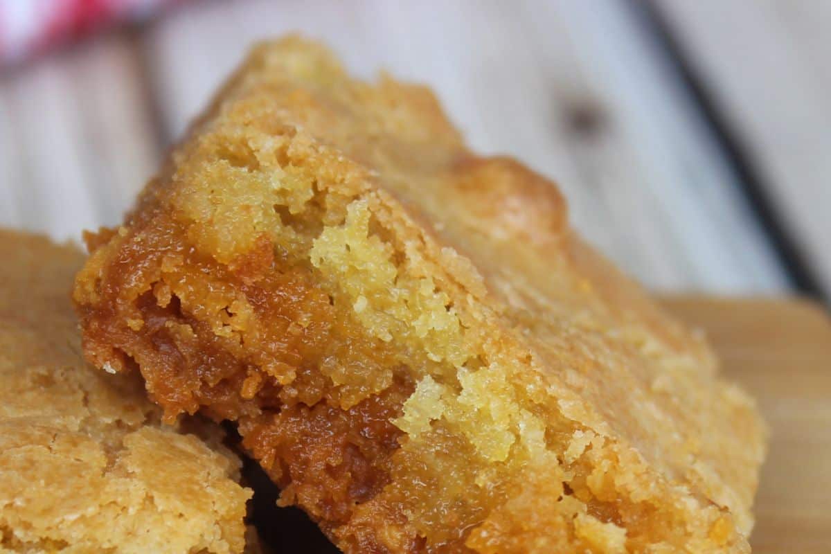 A close-up of two golden-brown blondie squares stacked on a wooden surface reveals their dense, crumbly texture, offering a glimpse into butterscotch recipes that are deliciously rich. Try today!.