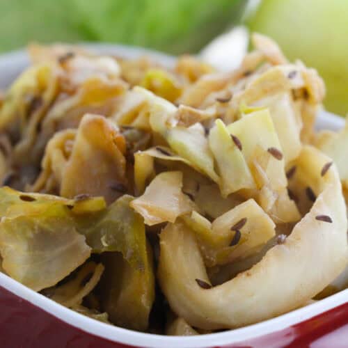 A close-up of Braised Cabbage with visible caraway seeds in a red and white dish.