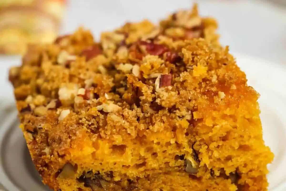 Close-up of a slice of deliciously rich pumpkin coffee cake topped with crumbly streusel and chopped nuts on a white plate. Try today!.