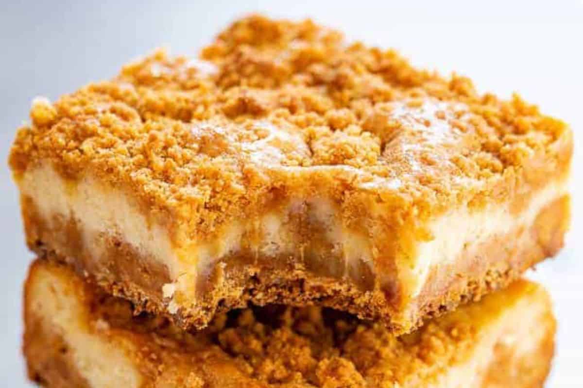 Two crumb-topped cheesecake bars stacked, showcasing a creamy filling and golden-brown crust, offer a delightful twist on traditional butterscotch desserts. With one bar teasingly bitten into, these treats promise a rich and delicious experience in every bite.