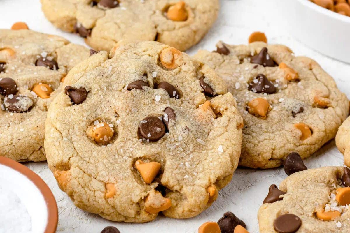 Close-up of chocolate and rich butterscotch chip cookies sprinkled with sea salt on a white surface.