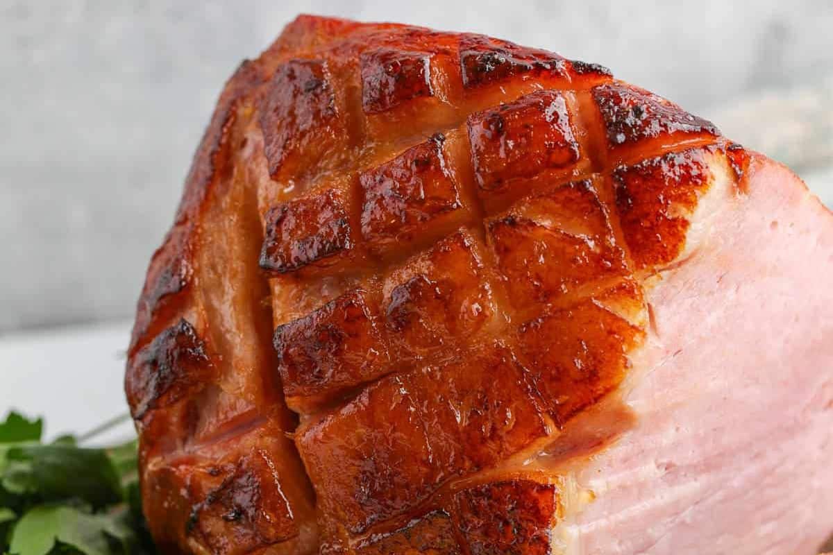This close-up shot captures the golden, crisscross-scored surface of a perfectly baked ham, lacquered with a citrusy glaze. Each caramelized square glistens, promising juicy, zesty flavor throughout. The rustic finish makes it feel both comforting and impressive.