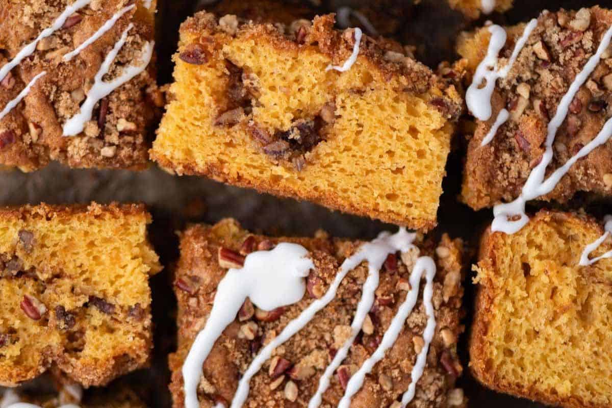 Close-up of a delicious pumpkin coffee cake, sliced and topped with streusel, a white icing drizzle, and chopped pecans—an irresistible delight you must try today!.
