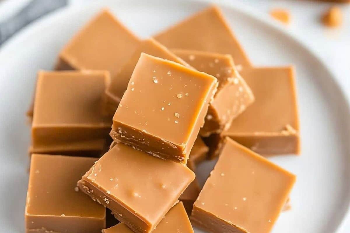 A plate with several neatly stacked pieces of caramel fudge, featuring smooth surfaces and a light brown color that highlights their deliciously rich flavor.