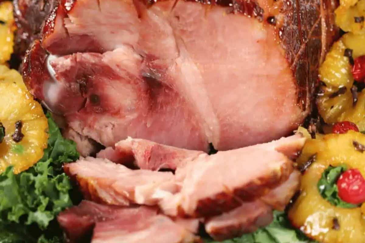 Sliced glazed ham surrounded by pineapple rings, cherries, and leafy greens—perfect for classic ham recipes and festive holiday gatherings.