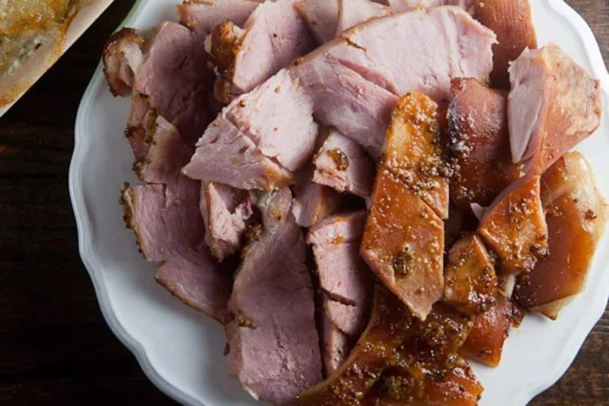 Sliced glazed ham arranged on a white plate, showing pieces of meat and crispy caramelized skin—a delicious choice for classic ham recipes or holiday ham recipes.