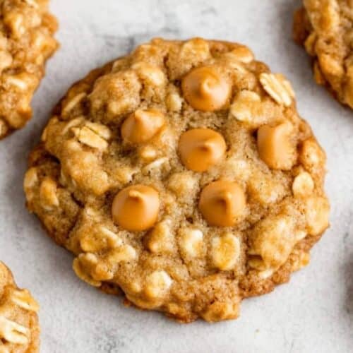 Close-up of oatmeal cookies with rich butterscotch chips on a gray surface. Five cookies are visible, showcasing their textured appearance.