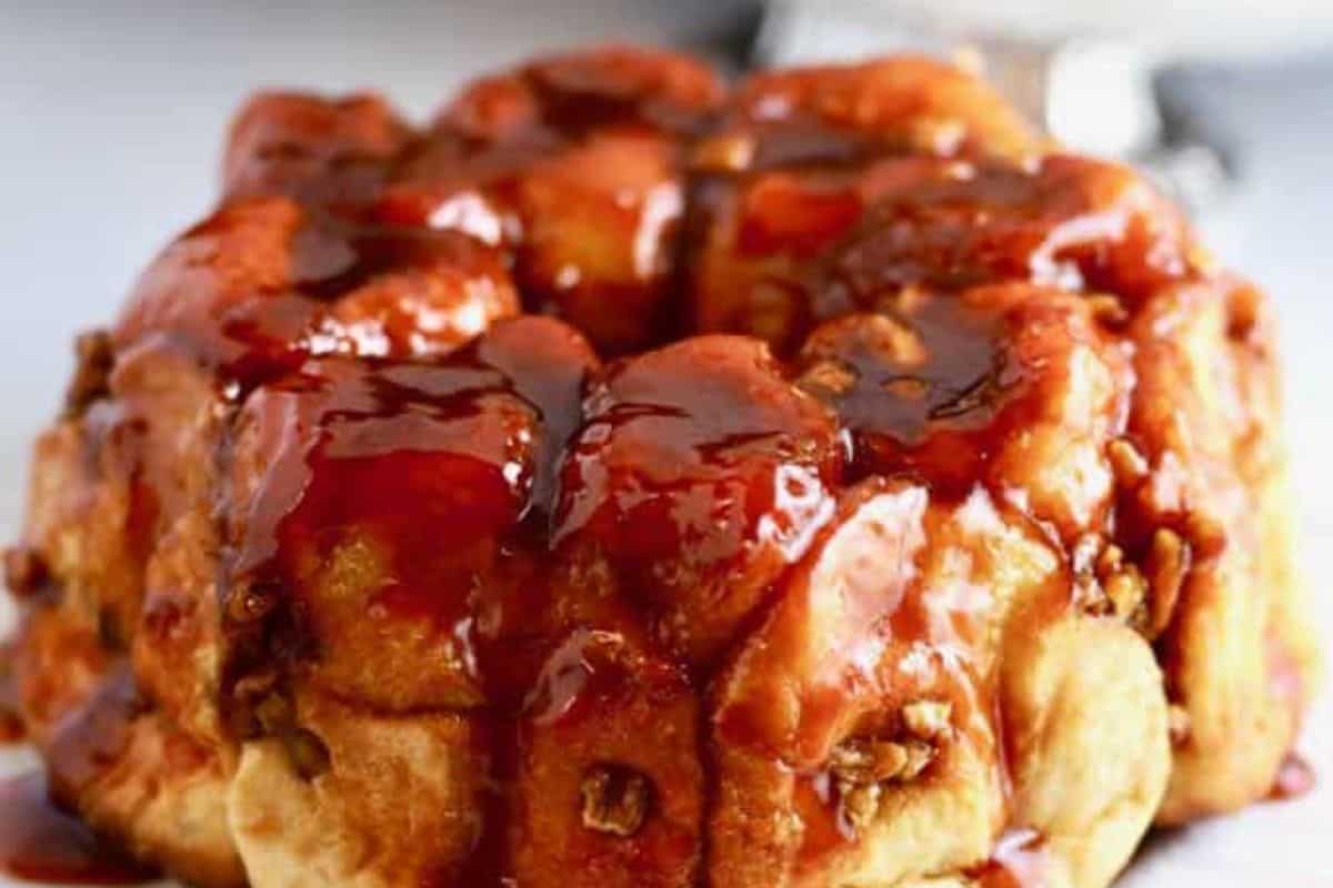Close-up of a glazed monkey bread with rich butterscotch sauce and nuts, arranged in a rounded shape on a white background.