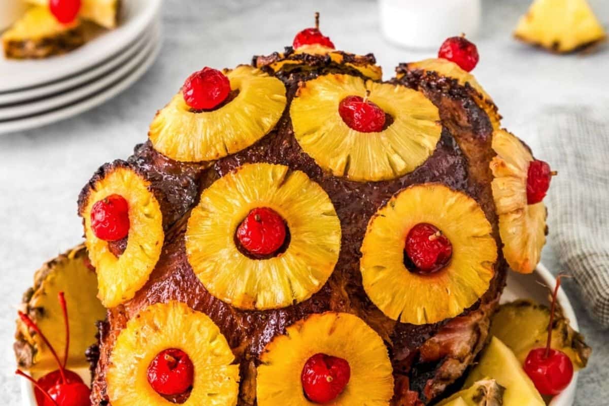 This picture-perfect ham is studded with golden pineapple rings and bright red cherries, giving off classic holiday vibes. The glossy glaze over the dark-crusted ham makes every detail pop. It’s a retro presentation that never goes out of style.
