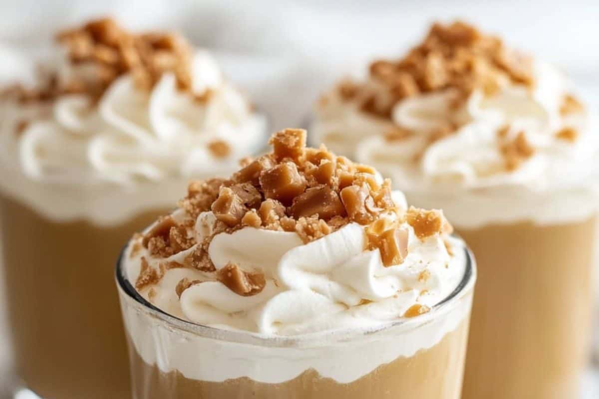 Three glass cups filled with a deliciously rich, creamy dessert are topped with swirls of whipped cream and delectable chunks of caramel toffee.