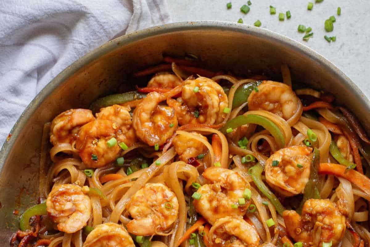 A skillet filled with shrimp, rice noodles, sliced bell peppers, and carrots, garnished with chopped green onions—a flavorful street food dish inspired by classic street food recipes.