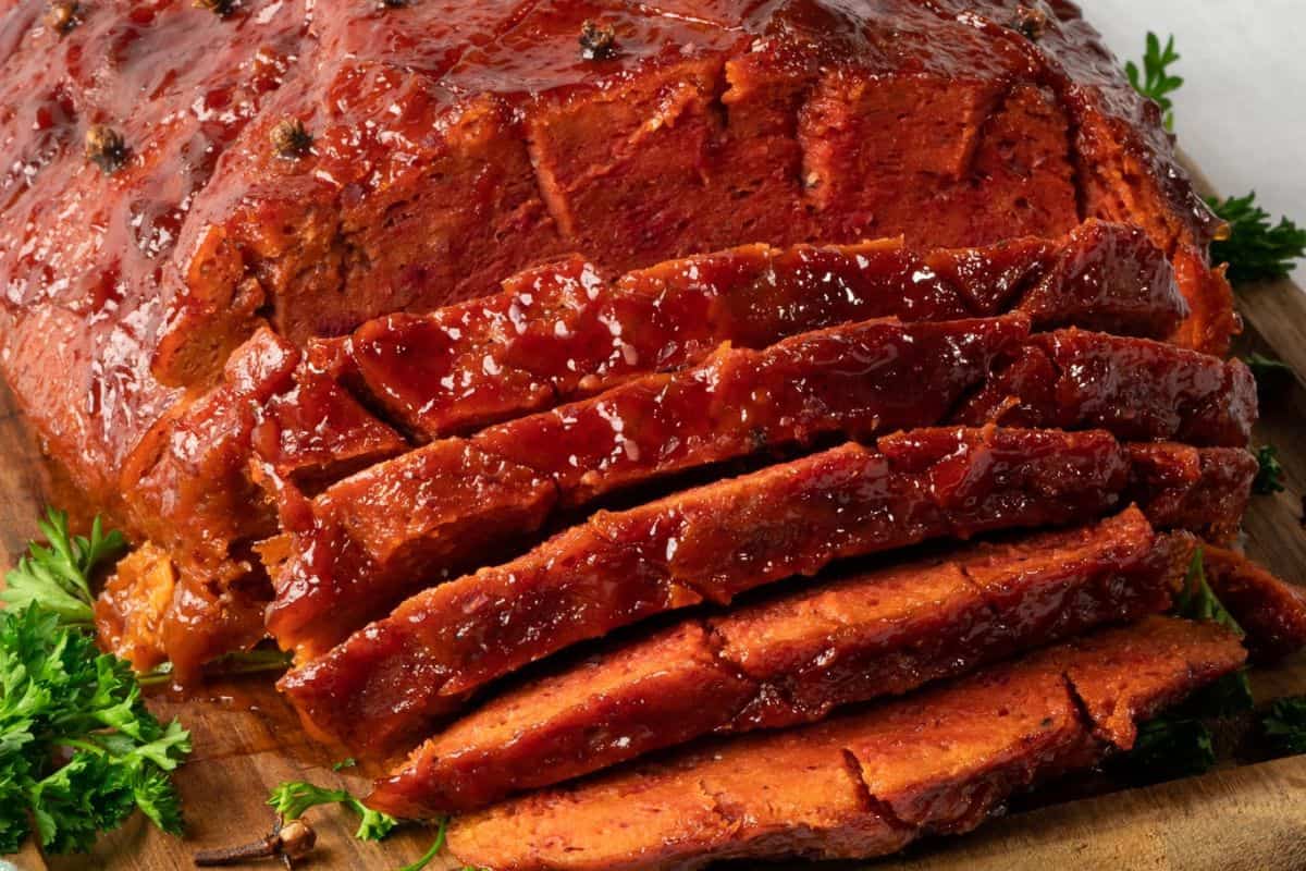 Sliced glazed vegan ham on a wooden cutting board, garnished with fresh parsley—a delicious twist on Holiday Ham Recipes.